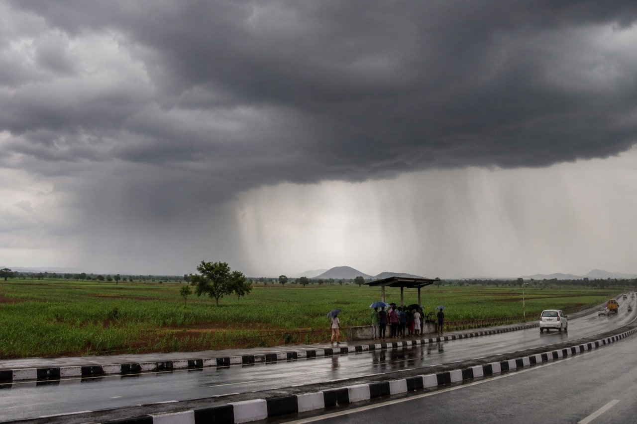 Dark monsoon clouds unleashing heavy rain over lush green farmland in central India as a farmer works in a flooded paddy field