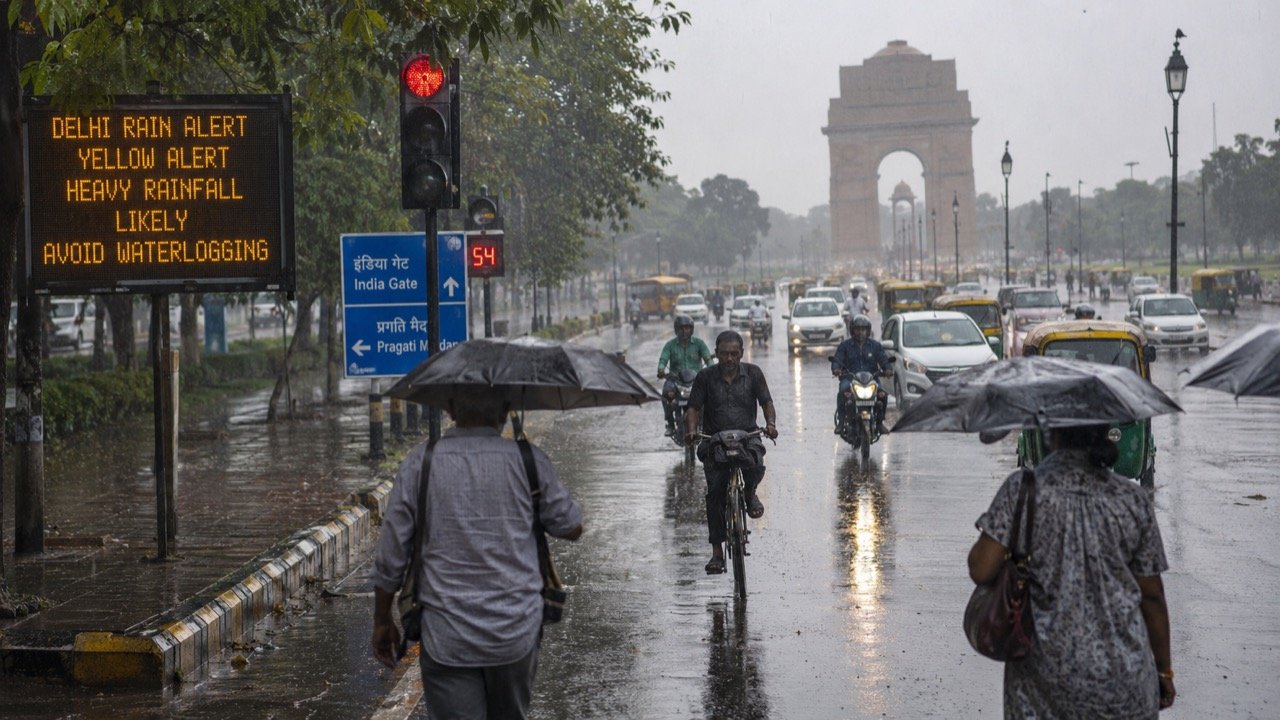 Heavy monsoon rain over a waterlogged Delhi road as commuters and auto-rickshaws navigate flooded stretches beneath dark grey skies
