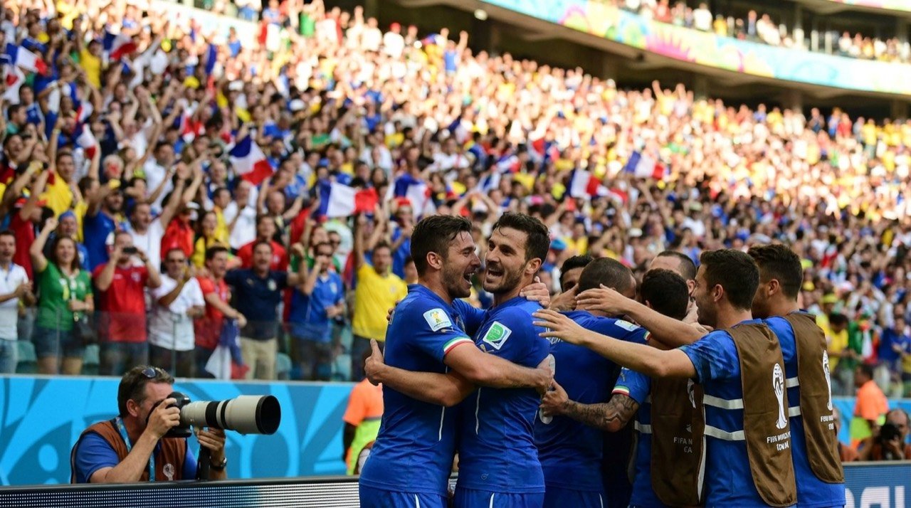 Footballers celebrating a goal during a FIFA World Cup group-stage match in a packed stadium.