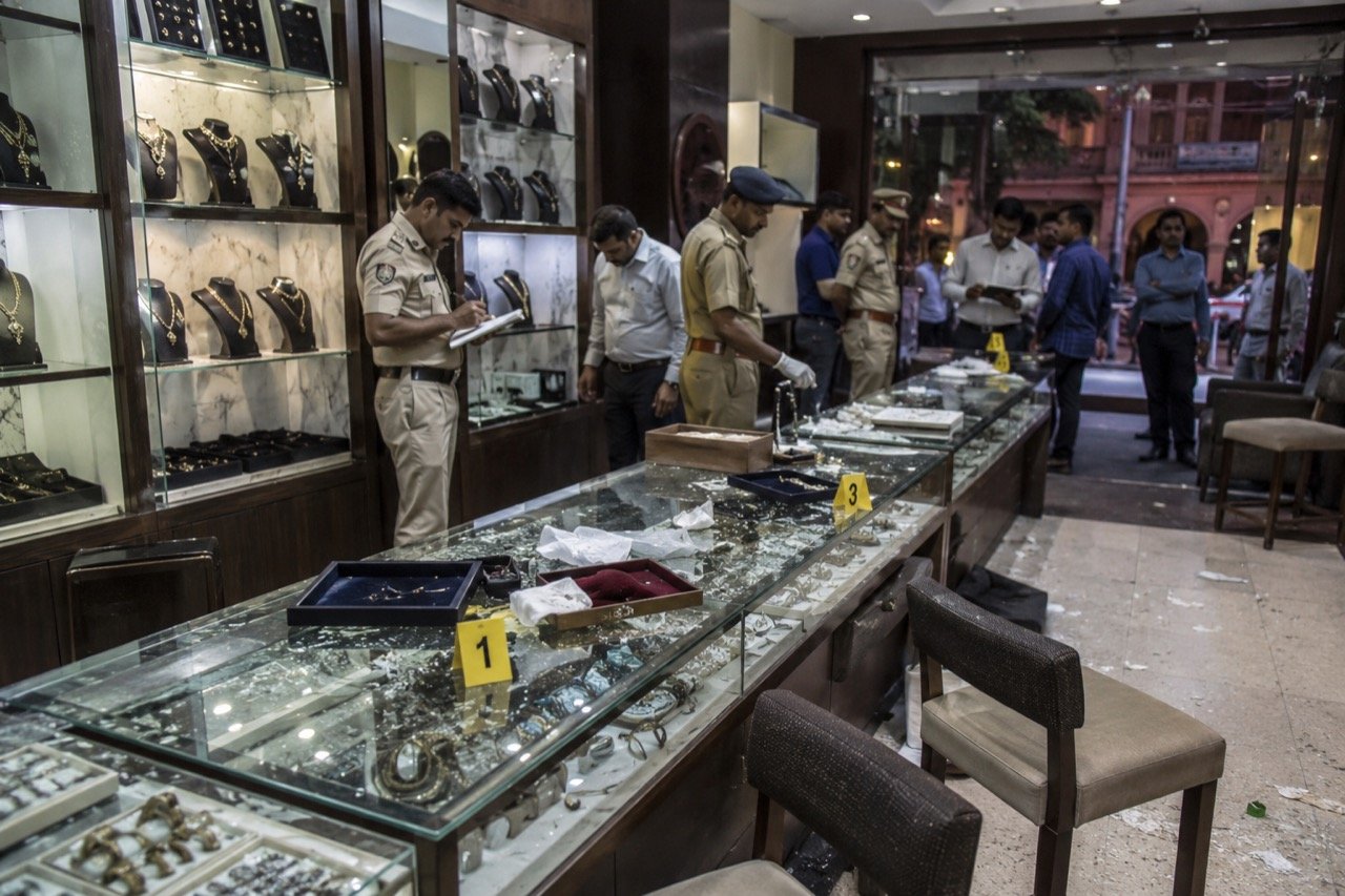 A jewellery shop in a busy Jaipur market street at dusk, its glass display cases glowing under warm lights as a police vehicle stands outside