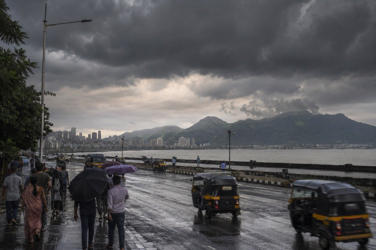 Dark monsoon clouds and heavy rain over a Mumbai street with commuters under umbrellas in June 2026
