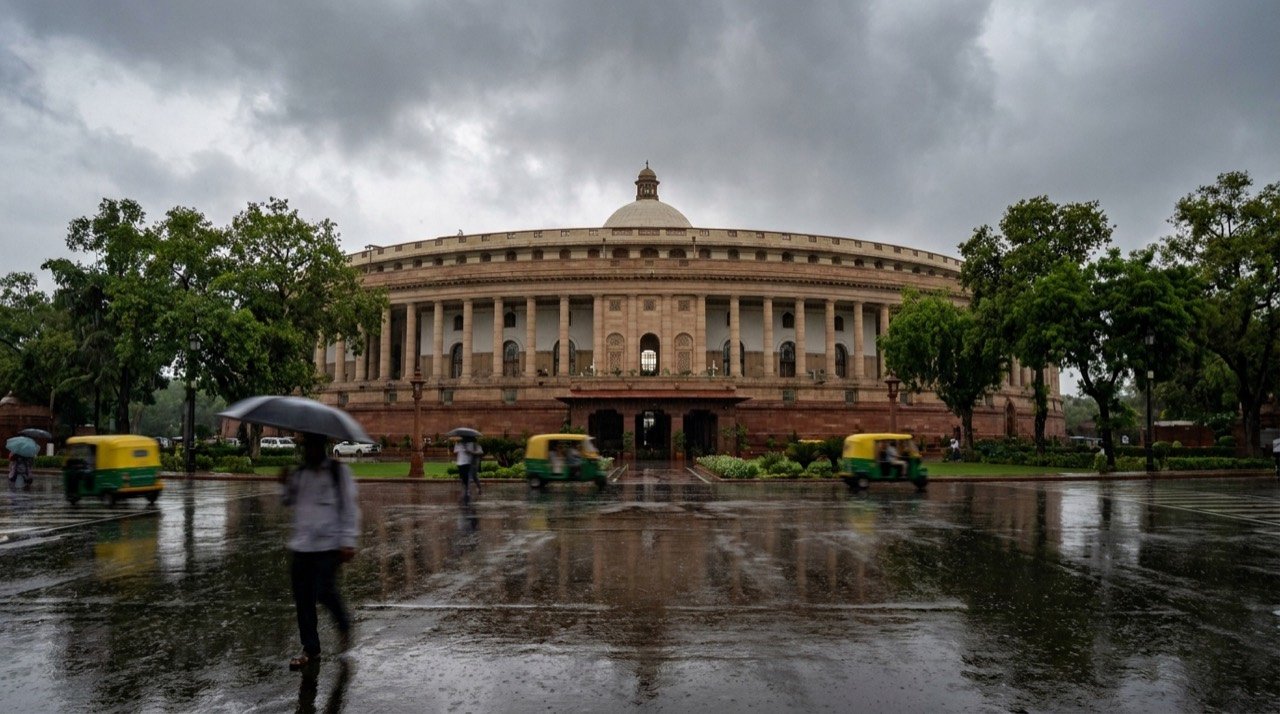 The Parliament House of India under a monsoon-clouded sky.