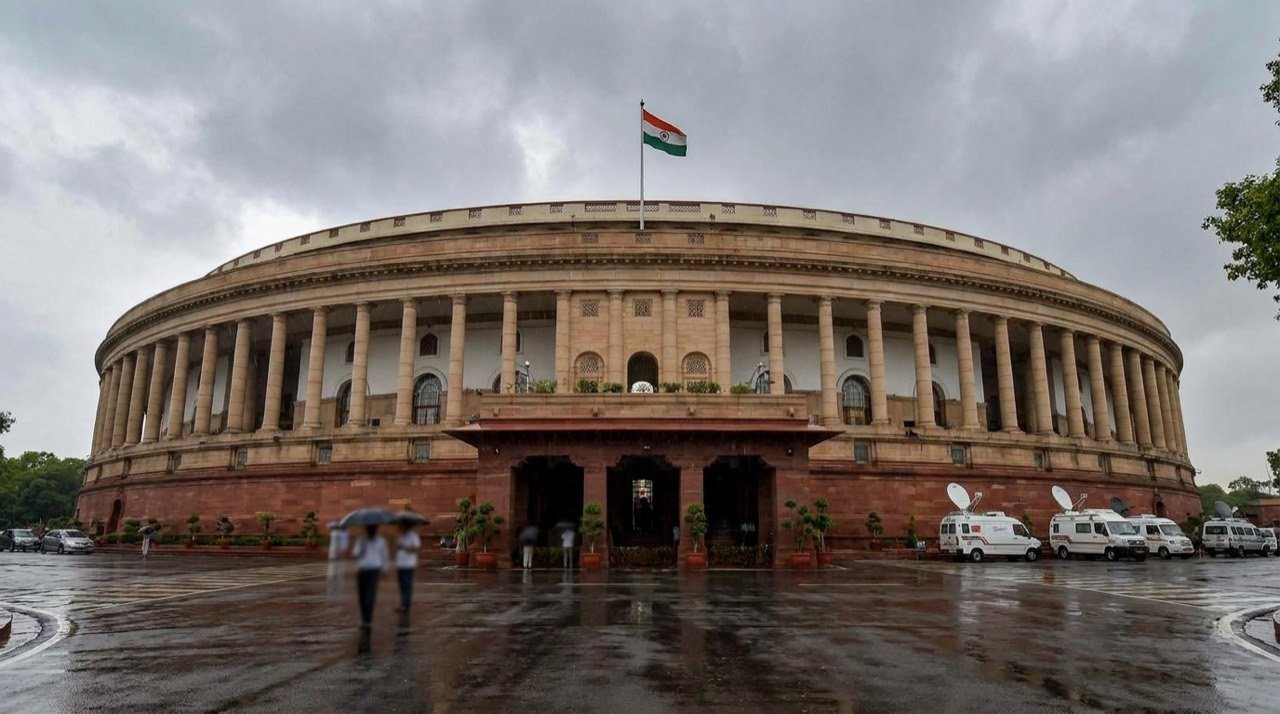 Wide view of the Indian Parliament building under a monsoon sky in New Delhi.
