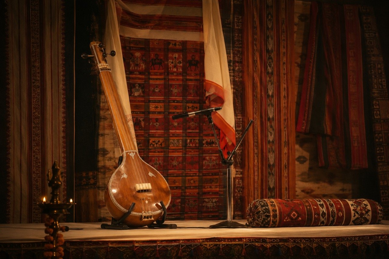A folk performer on a warmly lit stage holding a tambura aloft in a commanding storytelling gesture, draped in a traditional Chhattisgarhi sari, audience in soft shadow, 16:9 composition.