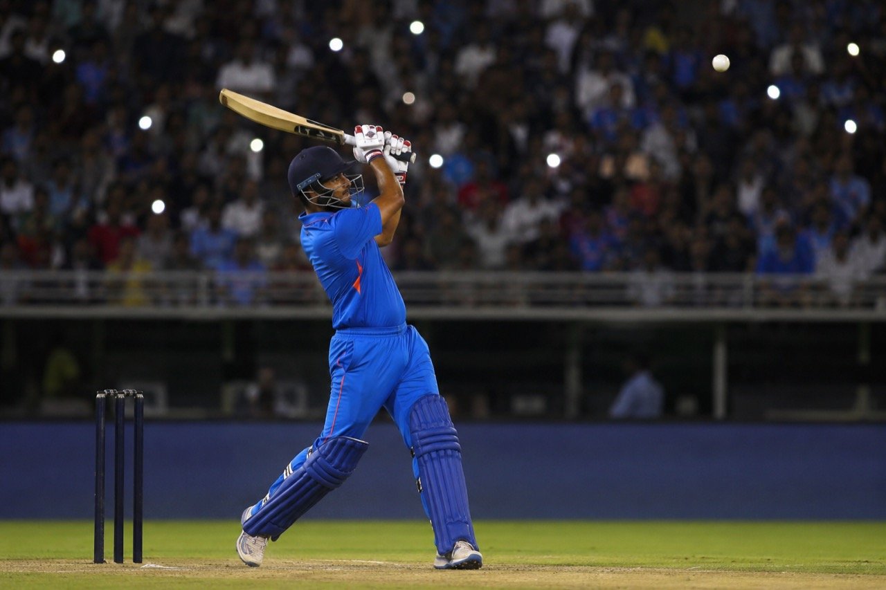A teenage Indian batter in blue T20 kit plays an aggressive lofted shot under stadium floodlights during a match against England